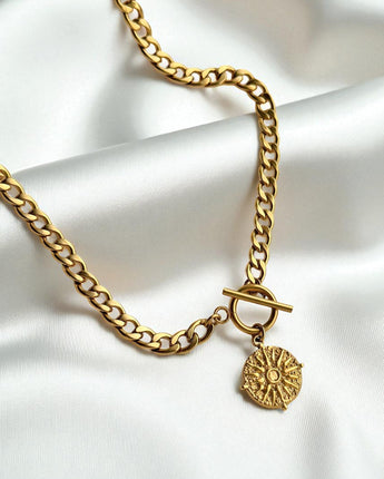 Gold engraved necklace with a round pendant on a white fabric background