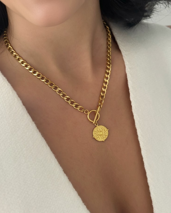 Gold engraved necklace with a pendant worn by a person in a white outfit.