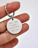 Keychain with 'DON'T LOSE YOUR FUCKING KEYS' text held by a hand on a white background