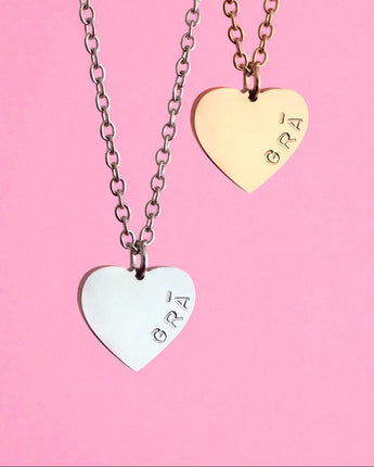 Two heart-shaped pendants on chains with 'GRA' engraving against a pink background